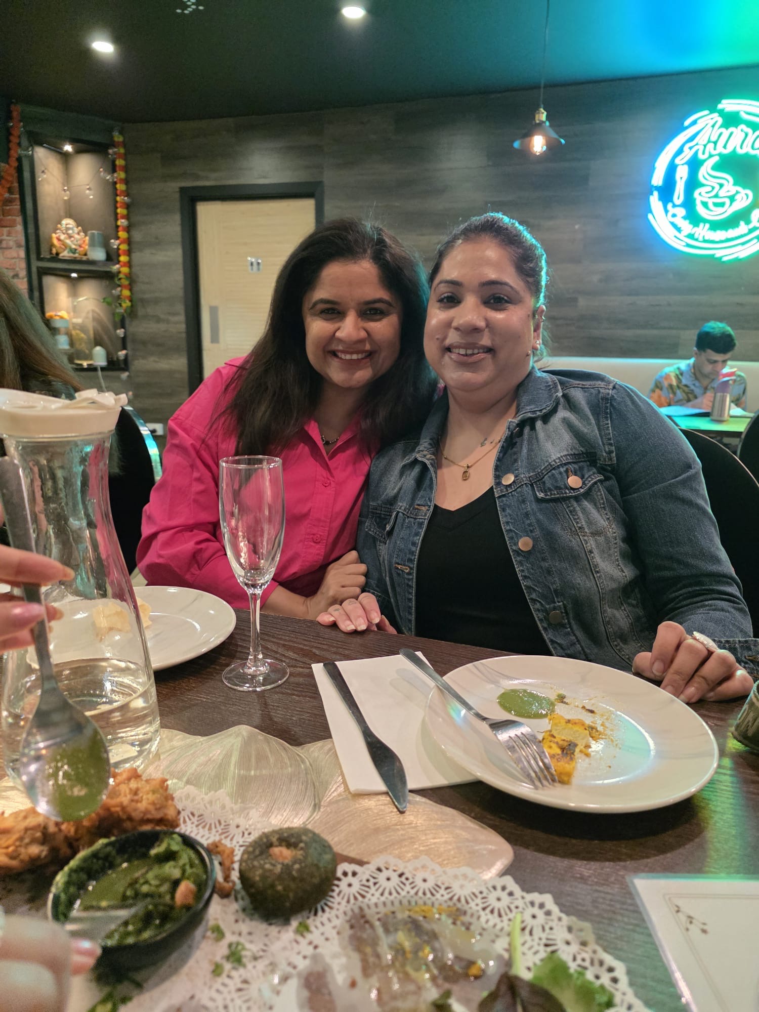 Two friends smiling together over dinner at Aura Indian Cuisine